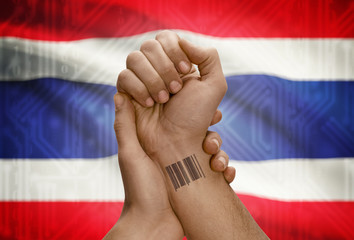 Barcode ID number on wrist of dark skinned person and national flag on background - Thailand