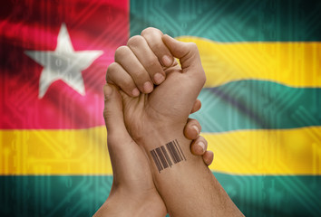 Barcode ID number on wrist of dark skinned person and national flag on background - Togo