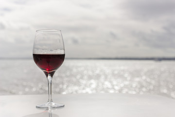 One glass of red wine with tears against tranquil sparkling sea water