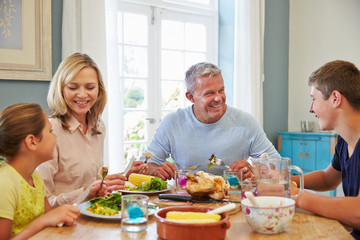 Family Sitting At Table Enjoying Meal At Home Together