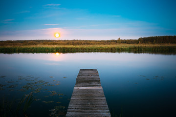 Moonrise over river lake pond in summer evening. Wooden boards p