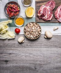 cooking pork steaks on the cutting board, on a napkin, mushrooms, spices, tomato border, place for text  on wooden rustic background top view close up