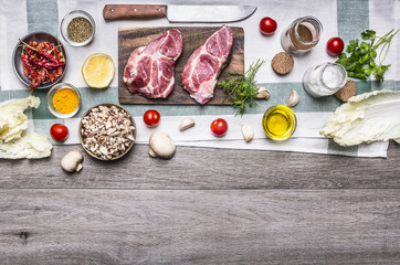 Ingredients for cooking pork steaks on the cutting board, on a napkin, vegetables, mushrooms, lettuce, spices and herbs on wooden rustic background top view border, place for text