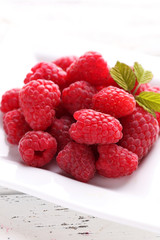 Red raspberries on plate on white wooden background