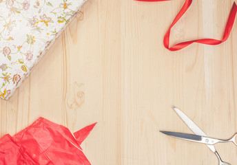 gift box, red paper, ribbon, scissors around empty space on wooden table