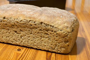 Homemade sourdough rye bread in baking form with background on wooden table