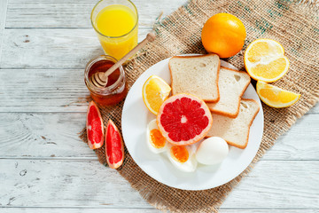 
Healthy diet breakfast, boiled eggs with white toast, fresh grapefruit and oranges , honey and orange juice on a wooden background