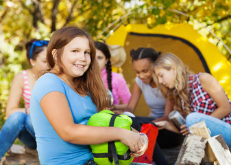 Cute girl holds sleeping bag sitting near camp