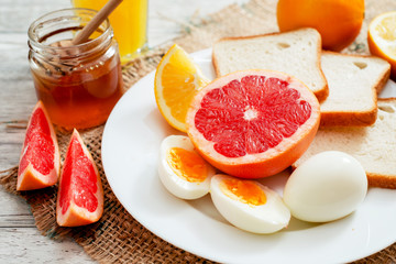 
Healthy diet breakfast, boiled eggs with white toast, fresh grapefruit and oranges , honey and orange juice on a wooden background