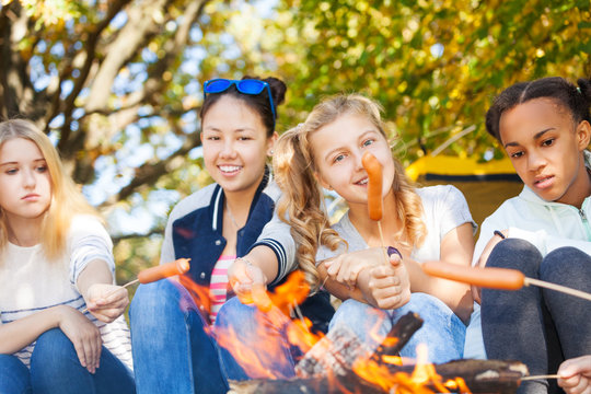Teen friends sit on campsite with sausages