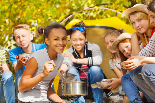 African Girl Cooks Soup In Pot At Campsite