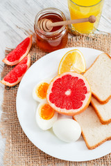 Naklejka na ściany i meble Healthy diet breakfast, boiled eggs with white toast, fresh grapefruit and oranges , honey and orange juice on a wooden background