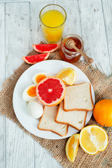 
Healthy diet breakfast, boiled eggs with white toast, fresh grapefruit and oranges , honey and orange juice on a wooden background