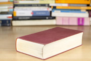 Red cover book on a clear wooden desk, with other books at background