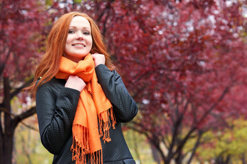 redhead girl in city park on red tree background, fall season