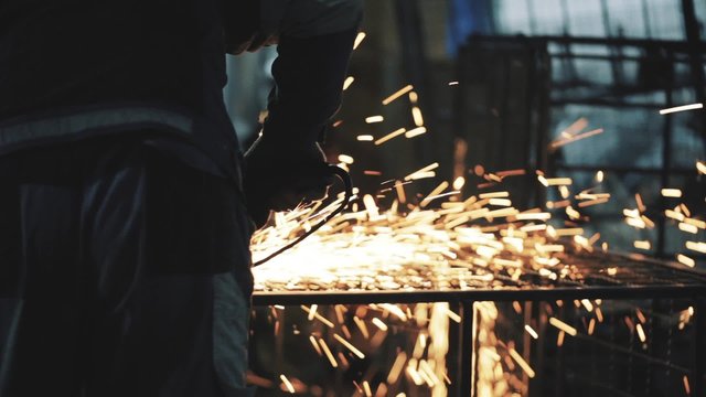 Man working on grinding / Man workpieces made of metal, a lot of sparks. Man protects the finished product from the metal