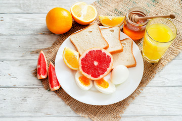 
Healthy diet breakfast, boiled eggs with white toast, fresh grapefruit and oranges , honey and orange juice on a wooden background