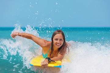Joyful young girl - beginner surfer with bodyboard has fun on small sea waves. Active family...