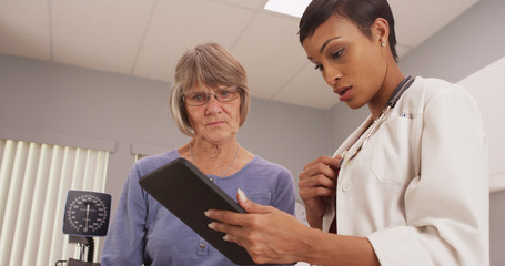 Fototapeta premium Young intelligent doctor looking at tablet with patient