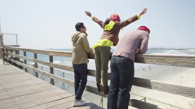 African woman reaching to the sky standing on pier with two multi ethnic men