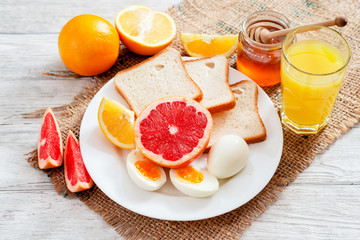 Naklejka na ściany i meble Healthy diet breakfast, boiled eggs with white toast, fresh grapefruit and oranges , honey and orange juice on a wooden background