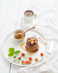 Breakfast set. Buckwheat pancakes with fresh garden strawberries, honey and cup of coffee over white wooden background