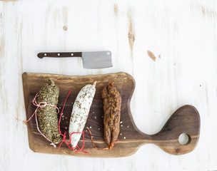 French alsacian smoked salamis on rustic walnut wooden chopping board over white backdrop, top view