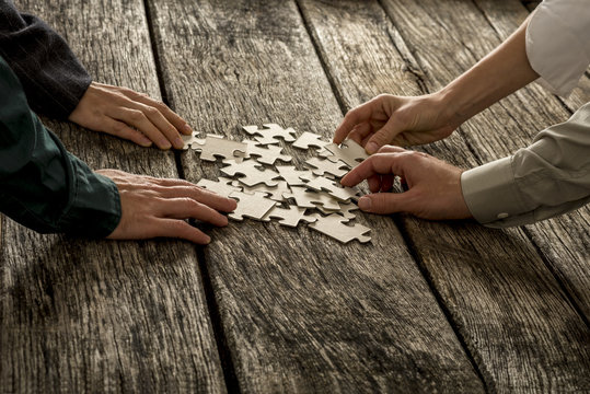 Pile of puzzle pieces lying on wooden desk with four hands reach