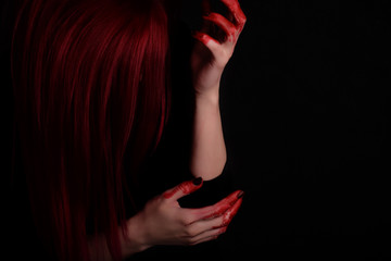 Woman with blood on hands and red hair against black background, unrecognisable
