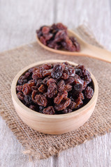 dry raisins in wooden bowl and spoon on white wooden table