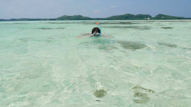 white woman snorkeling towards the camera, looking at camera, tropical island in the back	