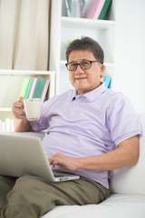 asian Senior Man Reading With Drink At Home