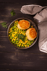 Chicken cutlets with vegetable garniture in metal skillet over wooden background, top view
