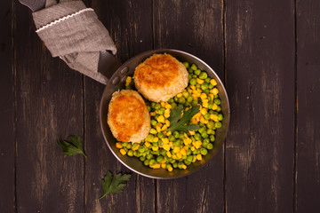 Chicken cutlets with vegetable garniture in metal skillet over wooden background, top view