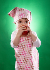 the baby girl with a kerchief and kitchen apron holding an vegetable isolated on the green background 