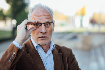 adult person with gray hair holding his eyeglasses, elegant dressed outside