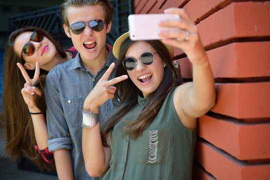 Young girls and boy having fun outdoor and making selfie with sm