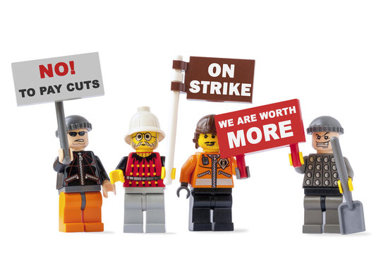 Workers on strike concept: four angry toy figurines isolated on white background and holding signboards