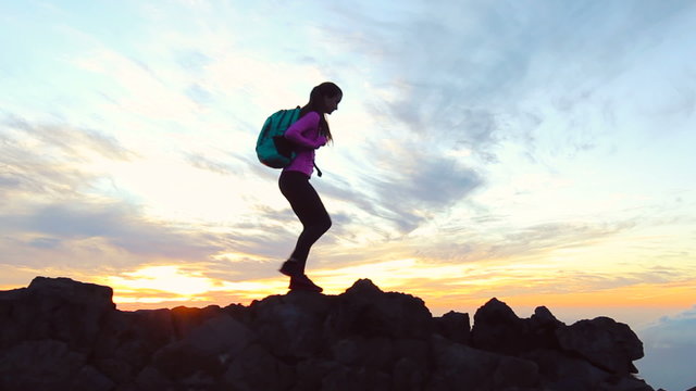 Hiker walks along narrow summit ridge crest at sunset. Reaching the Top. Young Woman Practicing Healthy Active Lifestyle.