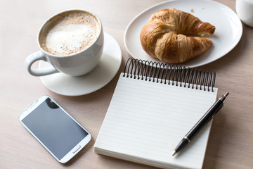 coffee, glasses , notebook , phone and croissant on a wooden tab