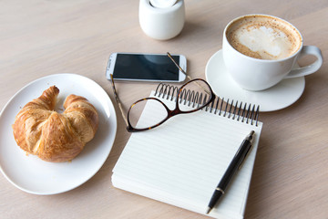 coffee, glasses , notebook , phone and  croissant on a wooden ta