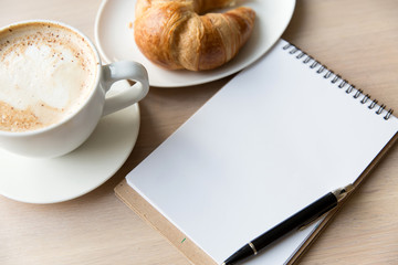 coffee , notebook  and  croissant on a wooden table
