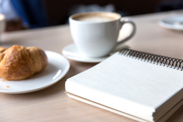 coffee , notebook and croissant on a wooden table