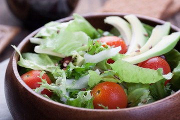 Salad with lettuce, tomatoes, flax seeds and avocado in a wooden bowl