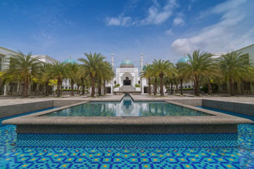 The white of Mosque Albukhary located in Alor Star, state of Kedah, Malaysia with its fountain and squares in the foreground and blue sky with clouds in the background.