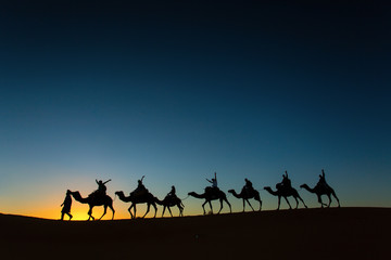 Sillhouette of camel caravan with happy peopple going through th
