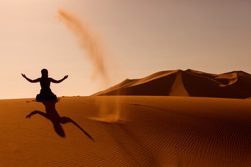 Sillhouette of woman playing and throwing with sands in Desert S
