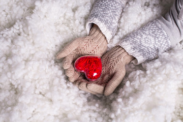 Obraz na płótnie Canvas Woman hands in light teal knitted gloves are holding beautiful entwined vintage red heart in a snow. St. Valentine concept.