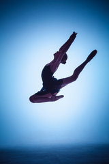 Obraz premium The silhouette of young ballet dancer jumping on a blue background