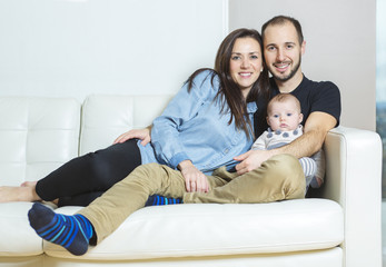 Handsome young father and mother with cute newborn baby on sofa